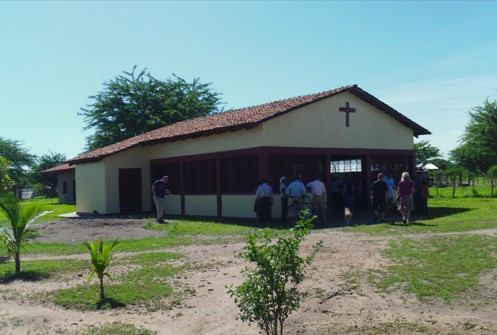 A cement block open-air church building with people from the village inside.